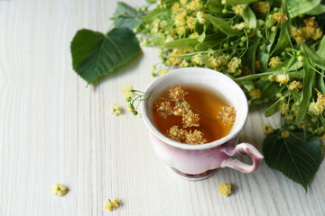 Cup of aromatic tea with linden blossoms on white wooden table, space for text