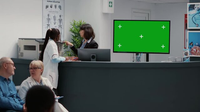 Monitor display with greenscreen background in hospital reception desk and waiting room lobby. Blank copy space with isolated chroma key and mock up template, tv screen. Tripod shot.