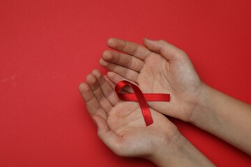 Little girl holding red ribbon on bright background, top view. AIDS disease awareness