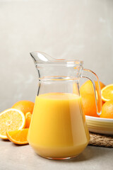 Jug of orange juice and fresh fruits on light grey table