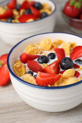 Bowl of tasty crispy corn flakes with milk and berries on wooden table, closeup