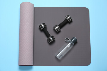 Exercise mat, dumbbells and bottle of water on light blue background, top view