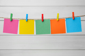 Clothespins with colorful blank notepapers on twine against white wooden background. Space for text