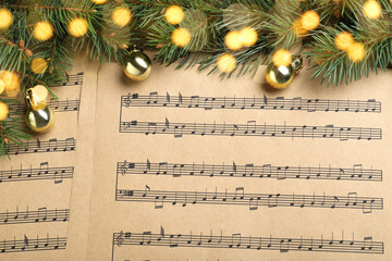Fir branches and golden balls on Christmas music sheets, above view