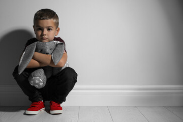 Sad little boy with toy near white wall, space for text. Domestic violence concept