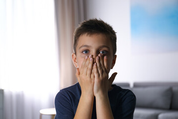 Abused little boy closing mouth indoors. Domestic violence concept