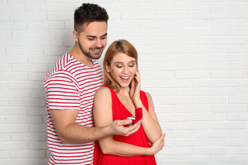 Man with engagement ring making marriage proposal to girlfriend near white brick wall. Space for text