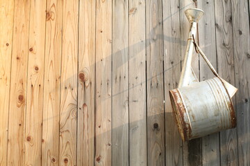 Old rusted metal watering can hanging on the brown wooden wall under sunlight. The concept of...