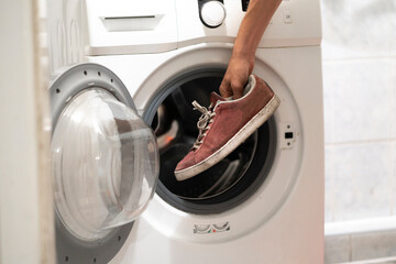 hands put dirty sneakers shoes in the washing machine
