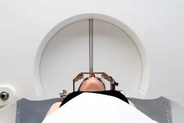 Foto op Aluminium The patient lies in front of the device for the treatment of cancer with a gamma knife. She has a metal clip cap on his head. Gamma Knife stereotactic radiosurgery. © ATRPhoto