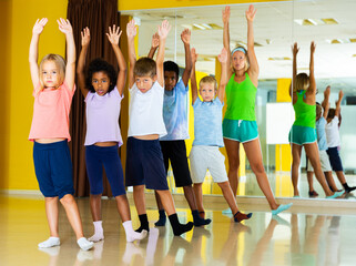 Group of tweens training movements of modern dance in choreography class with female tutor