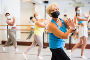 Fototapeta na wymiar Old lady dancing with other women in face masks during group training in studio.