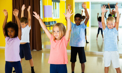 porttait of children dancing synchronous group choreography with female coach in dance hall