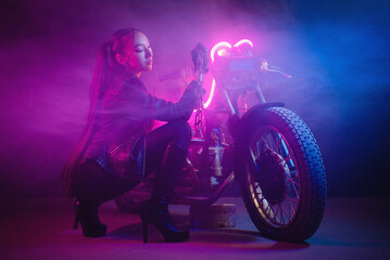 Naklejka na ściany i meble Beautiful asian girl a motorbiker with a chain in hand near the old motorcycle in the neon lights concept.