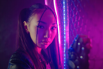 Beautiful asian girl near iron grid fence in the neon lights.