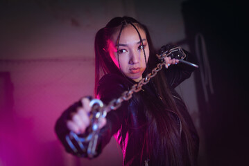 Beautiful asian girl with the chain in hands in the neon lights. Street fighter concept.