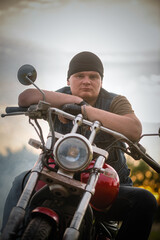 Motorbiker on the motorbike on the dusty empty countryside road at the sunset sun background. Motorcycle travel.