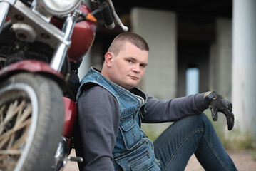 Obraz premium Motorcyclist is sitting near the motorbike outdoors.