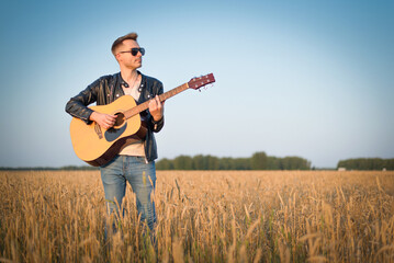 Musician with a guitar is walking among the wheat field.