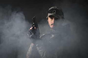A man with the airsoft rifle in the smoke on the dark background. Special agent concept. Action...