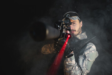 Futuristic soldier with a rifle on the black smoky background. Action movie film concept.