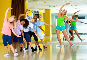 Happy cheerful preteen dancers practicing dance routine with female choreographer in modern studio.