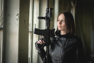 Young woman with the airsoft rifle is posing in the abandoned building. Action movie film concept. - obrazy, fototapety, plakaty
