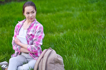 Young Asian woman Student with a book, notebook and pen on meadow. Preparation from session and exams. outdoor portrait