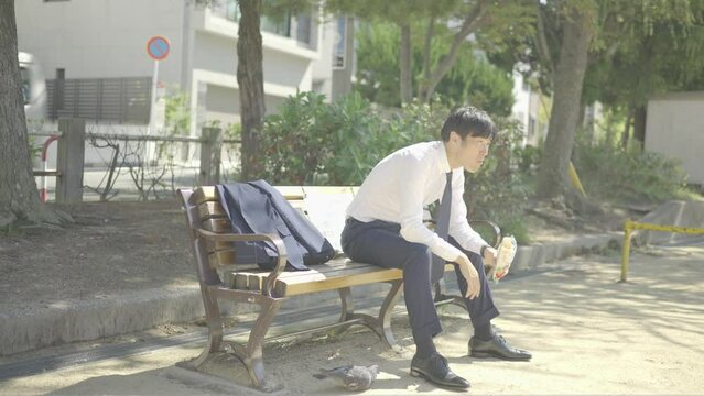 昼休みに公園でベンチに座ってパンを食べるビジネスマン