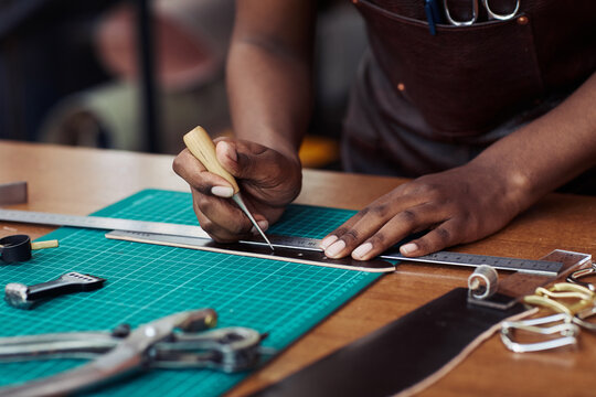 Closeup of black female artisan punching holes in handmade belt in leatherworking shop, copy space