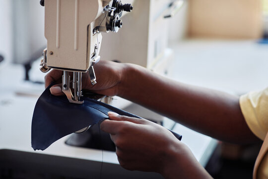 Side view close up of black young woman using sewing machine and creating handmade leather bag, copy space