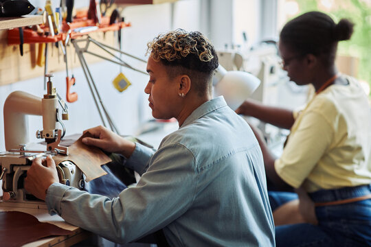 Side view of two women using sewing machines in leatherworking manufactory