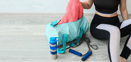 Young woman taking towel from sports bag while sitting on floor