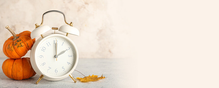 Alarm clock and autumn leaves with pumpkins on light background. Banner for design