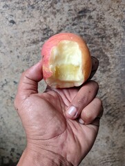 A man's hand holds a partially bitten apple 