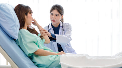 Asian young professional female practitioner doctor in white lab coat with stethoscope holding touching checking monitoring patient injury arm and muscle while laying down on bed in hospital wardroom