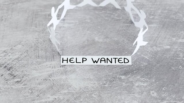 staff shortages and business struggling after the pandemic, peper people chain with Help Wanted text on gray background