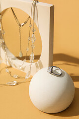 Showcase pedestals with elegant diamond ring and necklace on beige background, closeup
