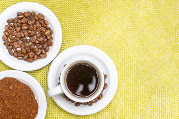 Top view of a cup of coffee served with beans and powder on ceramic plates on a green table