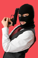 Young woman in balaclava posing with gun on red background