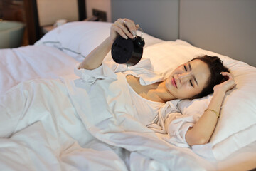 Happy young asian woman in white lingerie lying in bed, wake up late and overslept morning, trying...