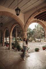 A young woman is standing near beautiful building with arch and potted plants