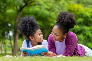 African American mother is teaching her young daughter to read while lying down after having a...