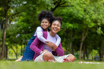 African American mother is playing piggyback riding and hugging with her young daughter while...
