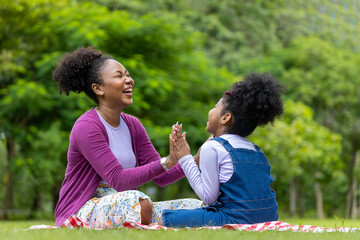 African American mother is laughing while playing patty cake with her young daughter while having a...