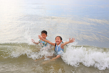 Cheerful Asian little boy and young girl child enjoy playing and lying on tropical sea beach at sunrise. Adorable sister and brother having fun in summer holiday.