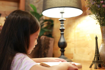 Close-up little Asian girl child in casual clothes reading a book and smiling on the desk in the room.