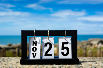 Nov 25 calendar date text on wooden frame with blurred background of ocean.