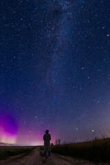 abstract night photo of a figure of a lonely person in a field under a starry sky and northern lights, starfall. Astrophotography
