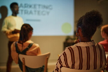 Back view of young black woman listening to business coach while sitting in audience in training...